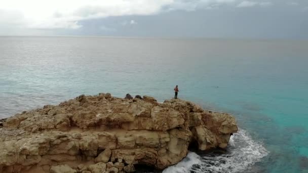 青の海の真ん中の岩の上に立つ若くてスタイリッシュな旅行ブロガーの写真家 ラグーンだ 空中写真 — ストック動画