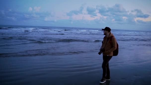 若いスタイリッシュな旅行ブロガーの写真家が海辺や海を歩いています 走っている男の前で風景を撮る — ストック動画
