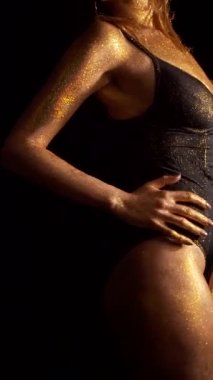 Siyah arka planda altın tenli kız vücudu. İç çamaşırlı seksi kadın elleriyle vücudunu okşuyor.