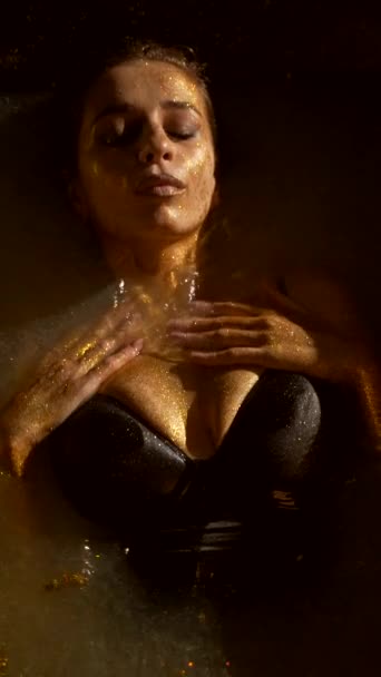 特写兴奋的女人躺在水里摸着她的乳房 全身都是金色的染料 黄金皮革 女孩躺在浴缸里 垂直框架 — 图库视频影像