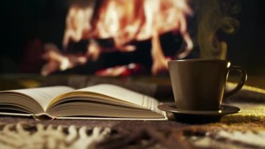 Açık kitap ve yanan şöminenin yanında bir fincan kahve ile Hygge konsepti. Kahve havası. Geçmişi. Rahatlama zamanı. 4K