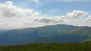 Güneşli bir öğleden sonra. Dağlardaki harika bahar manzarası. Çimen tarlaları ve yuvarlanan tepeler. Mavi dağların arka planında. Yeşil otlarla kaplı yeşil alp dağları. bahar Havacılık Görünümü