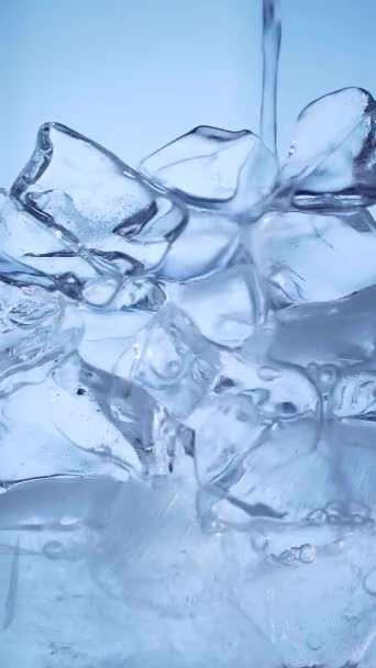 ガラスに氷と泡でソーダ水を入れてください 接近速度の遅い動きだ 透明ブルーの背景に爽やかで新鮮なミネラルウォーター マクロだ アイスキューブウォッカ テキーラ 垂直ビデオフレーム — ストック動画