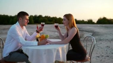 Genç bir çift doğada bir masada oturuyor. Gün batımında kumlu sahilde ilk romantik randevu. Şarabı seviyor, gülümsüyor. Açık havada. Siyah elbiseli kızıl saçlı kız. Genç adam.