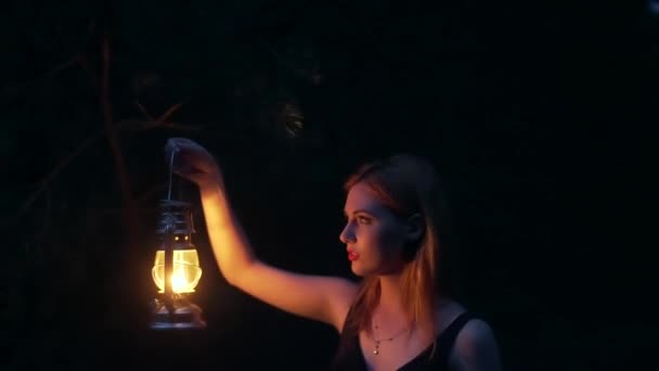 ケロシンランプのある神秘的な森の少女 暗い森の中で懐中電灯のろうそくや光と夜の黒いドレスの女性 若い者は木の間で道に迷った 危険な幻想的な光 — ストック動画