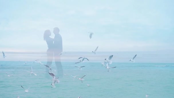 加倍暴露 慢动作年轻的恋人在海浪上的轮廓和飞翔的鸟儿 海鸥在大海中飞翔 背景是一群年轻人紧紧拥抱在一起 穿着黑色衣服 — 图库视频影像