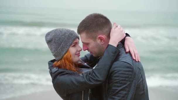 爱的年轻夫妇站在海边亲吻 海景背景下的海岸 冬天或秋天的风寒冷的天气雨 恋人跳舞拥抱 互相微笑 走在鸟儿身上 — 图库视频影像
