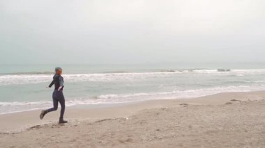 Siyah elbiseli ve deri ceketli genç kız. Kaçar, okyanus ya da deniz kenarındaki kameraya güler. Kış ya da sonbahar, soğuk hava, kum dalgalarının arka planına karşı ağır çekim. Mutlu.