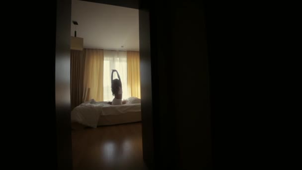 一个女孩的轮廓 伸展在窗户的后面 早上在卧室或宾馆醒来 床白色 迷人的女人后视镜 阳光灿烂 — 图库视频影像
