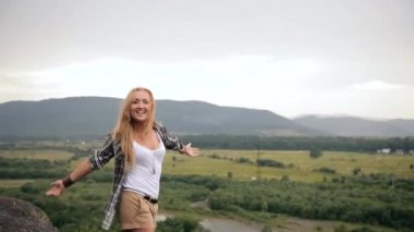 Dağın tepesinde kollarını kaldırıp kollarını havaya kaldırmış, mutlu ve sarhoş bir genç kız hippi gezgin. Yağmur, rüzgar, nehrin arka planındaki tişörtü havaya uçuruyor.