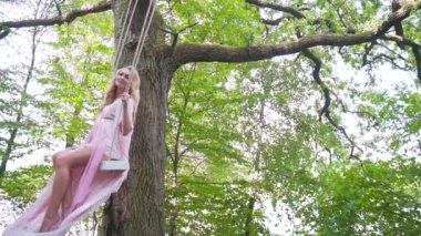 Zarif elbiseli genç bayan. Bir salıncakta oturuyor. Bulutlarda ya da dumanda. Ağaçtaki orman muhteşem mistik bir manzara. Pembe sinekler esiyor. Romantik, tasavvur edilmiş, mutlu kız rüyaları. Peri masalı prenses rüyası.. 