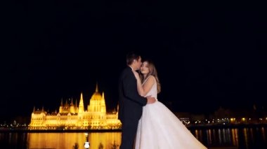 Düğünde genç ve sevgi dolu bir çift. Eski gece şehrinin arka planında birbirlerine sarılıyorlar. Budapeşte Macaristan 'daki parlamento binasında aydınlandı. Avrupa. Gece kalenin ışıkları. Yavaş çekim