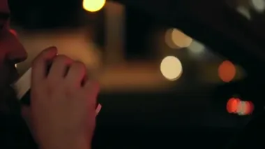 Yakın plan portre. Araba süren ve kahve içen genç, vahşi bir adam. Kahve fincanı. Bulanık ışıkların ve gece şehrinin arka planına karşı. Renkli bokeh. Ağır çekim. koyu siyah arkaplan