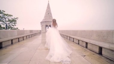 Moda mankeni, uzun bir gelinlik içinde gelin arkadan ve dışarıdan, koşuyor ya da yürüyor, etrafına bakıyor. Eski kasaba ve şatonun mimarisinin arka planına karşı.