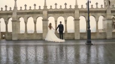 Genç çift el ele tutuşup eski şatonun ve şehrin mimarisini geçti. Baluster kemer, harf ve vintage sütunlarının arka planında. Tarihi bir yer. Lüks moda, gelin ve damat  