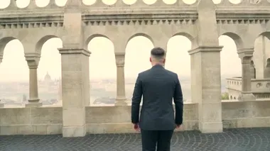 Siyah takım elbiseli, ceketli genç çekici bir adamın portresi eski şehir arka planında, şatoda, taş bina mimarisinde kemer ve sütunlarla gider. Lüks, zarif, sofistike, erkek, erkek. 