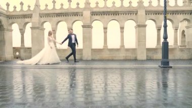 Genç çift el ele tutuşup eski şatonun ve şehrin mimarisini geçti. Baluster kemer, harf ve vintage sütunlarının arka planında. Tarihi bir yer. Lüks moda, gelin ve damat  