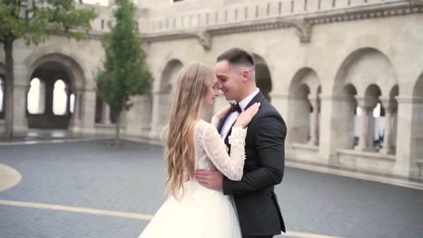 portrait of young wedding couple, against old city background, historic castle, and architecture, outdoors the bride hugs the groom leaning against each other, kissing stroking, luxury wedding fasion