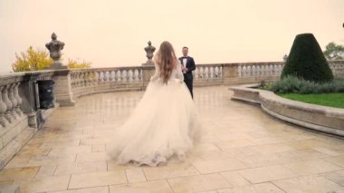 Gelin damada koşar, eski kalenin meydanında, eski kasabanın beyaz arka planı, uzun açık renk saçlar. Bali Malikanesi ve Baluster Sarayı. Yavaş çekim.