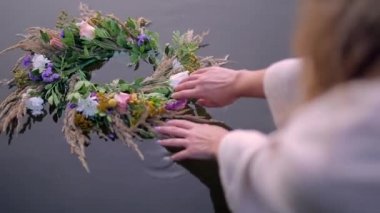 Bir kızın yakın çekimi suya çiçek ve şifalı otlardan oluşan bir çelenk düşürür. Ivan Kupala 'da nehrin ya da gölün yakınında bir kadının elleri. Bir buket kır çiçeği ve kurumuş ot. Kadın sırtı ve sarı uzun saçlar.
