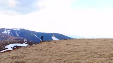  Harika bir hava manzarası var, gelin damada yaklaşıyor. Beyaz bir gelinlik içinde. Güzel dağların arka planında duruyor. Düğün çifti sarılıp öpüşüyor. Karla kaplı kayanın tepesinde.