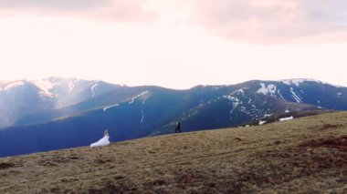 Gelin damadın elini tutuyor, düğün çifti birbirine doğru koşuyor ve birbirlerine doğru yürüyorlar, bir dağın tepesinde, doğanın muhteşem manzaralarıyla. Mavi gökyüzü ve kayalar, gökyüzü manzarası