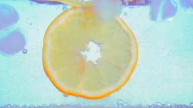 Kapatın. Bir dilim limon ya da portakal, buzlu karbonatlı soda suyuna düşer. Bir bardak maden suyunda. Ağır çekim. Makro. açık mavi beyaz arkaplan.
