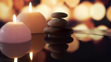 Kapatın. Yanan mumların rahatlatıcı görüntüsü. Bulanık arkaplanda su yansıması olan taşlar. Yanan mumlar. Rahatlama, meditasyon, huzur ve sessizlik..