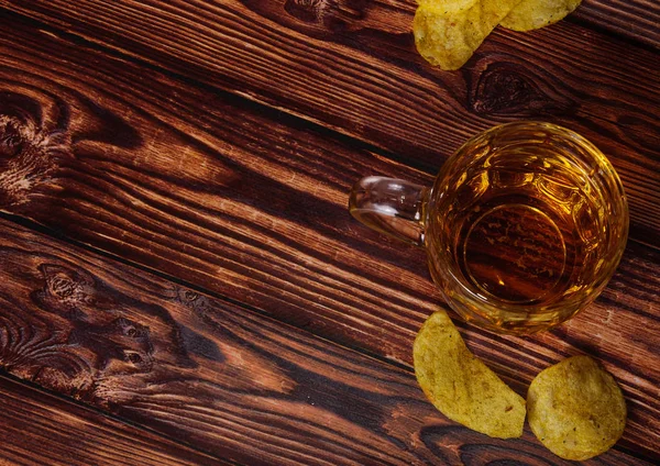 A glass of fresh beer and potato chips on a wooden wooden table — Stock Photo, Image
