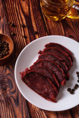 Bir bardak bira ahşap arka plan üzerinde beyaz bir plaka üzerinde taze basturma