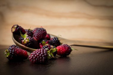 Tahta kaşıkta böğürtlenler siyah bir masanın üstünde. 