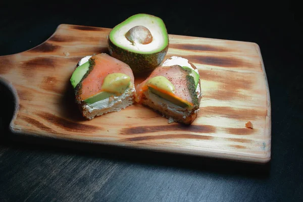 smoked salmon toast on a bed of avocado and fresh cheese, with a touch of ground pepper and parsley