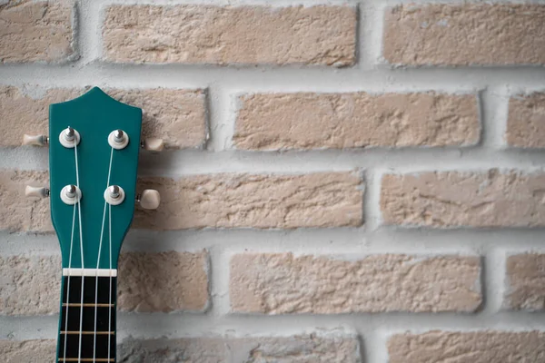 Ukulele green guitar over brick wall beige background with copy space
