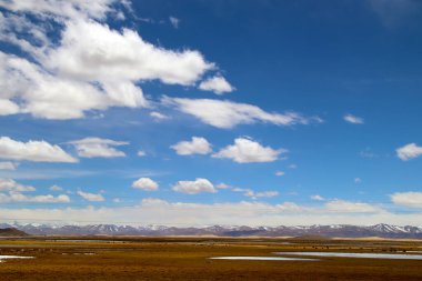 Qinghai-Tibet Platosu 'ndaki araziler, mavi gökyüzü ve beyaz bulutlar altında, sulak alanlar, otlaklar, çöller ve buz gölleri kesişiyor.