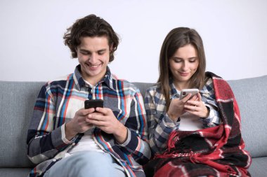 Kanepede oturan ve akıllı telefon kullanan neşeli çiftin ön görüntüsü.