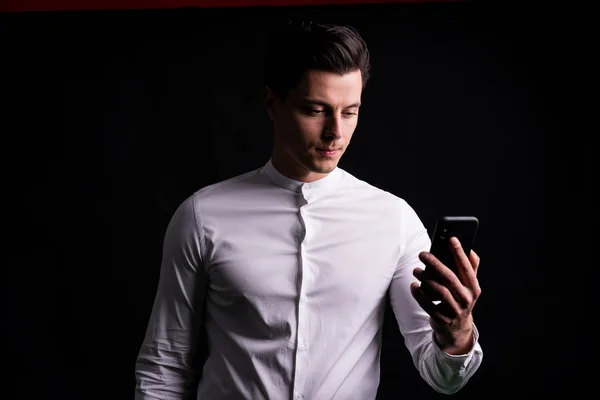 Il tipo con il telefono in mano che si fa un selfie o parla con gli amici. Sfondo nero nello Studio — Foto Stock