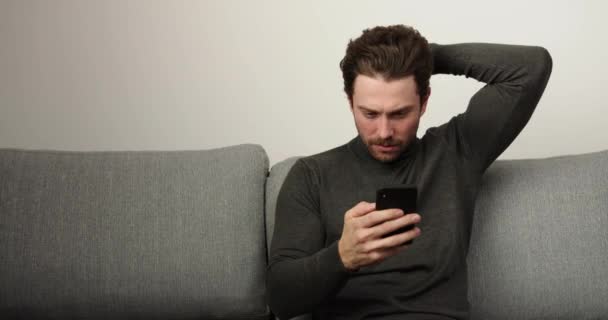 O homem fala ao telefone. Corte de cabelo elegante e um bom visual. Homem sentado no sofá em casa na sala de estar e conversando com os amigos . — Vídeo de Stock