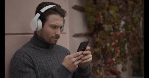 Glücklicher Mann mit Telefon in der Hand. Musik über den Kopfhörer hören und mit dem Handy telefonieren — Stockvideo
