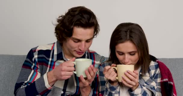 Glada par sitter på soffan i vardagsrummet och dricker varmt te med leende — Stockvideo