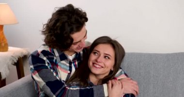 Oturma odasında kanepede oturmuş kız arkadaşını kucaklayan ve öpen genç adam.