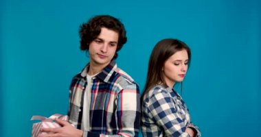 Hediye sunan ve öpüşen erkek, mavi arka planda izole edilmiş, alıngan kız arkadaş.