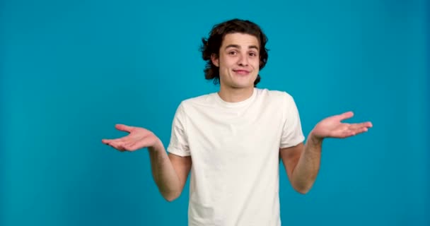 Front view of confused young man showing shrug gesture isolated on blue background — Stock Video