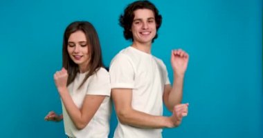 Beyaz tişörtlü neşeli bir çift birbirlerine bakıyor, mavi arka planda izole edilmiş bir gülümsemeyle dans edip el ele tutuşuyorlar.