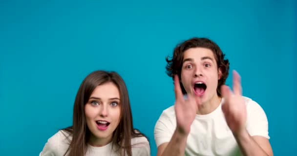 Geschokt koppel kijken naar camera, geven high five aan elkaar en tonen ja gebaar geïsoleerd op blauwe achtergrond — Stockvideo