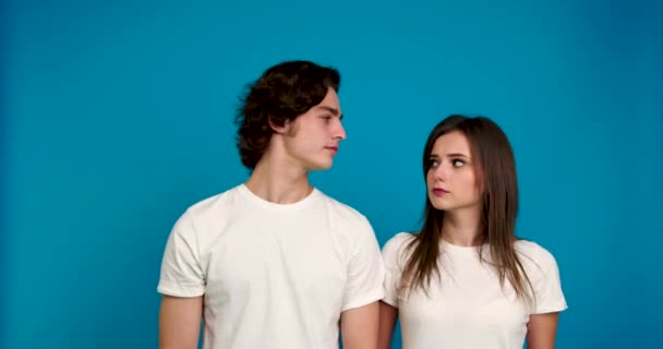 Pareja en camisetas blancas mirándose y riendo aislados sobre fondo azul — Vídeos de Stock