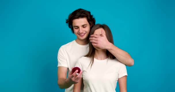 Man covering eyes to girlfriend, showing weding ring, kissing and embracing isolated on blue background — Stock Video