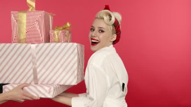 Laughing pin up girl holding present boxes on pink background — Stock Video