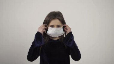 Çekici bir kızın tıbbi maske takıp kameraya baktığı ön manzara.