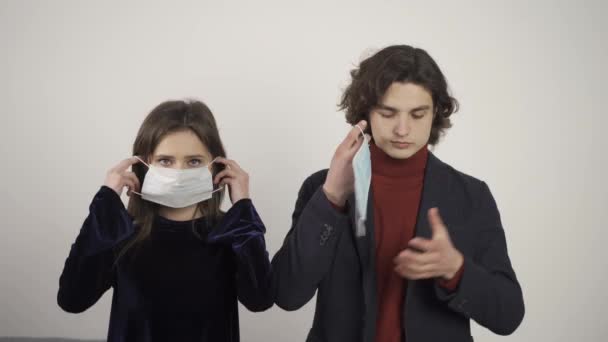 A fiatal férfi és nő orvosi maszkot visel, és a kamerába néz. — Stock videók