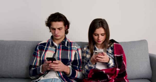Gelukkig paar zit op de bank, met behulp van smartphones en glimlachen in de woonkamer — Stockvideo